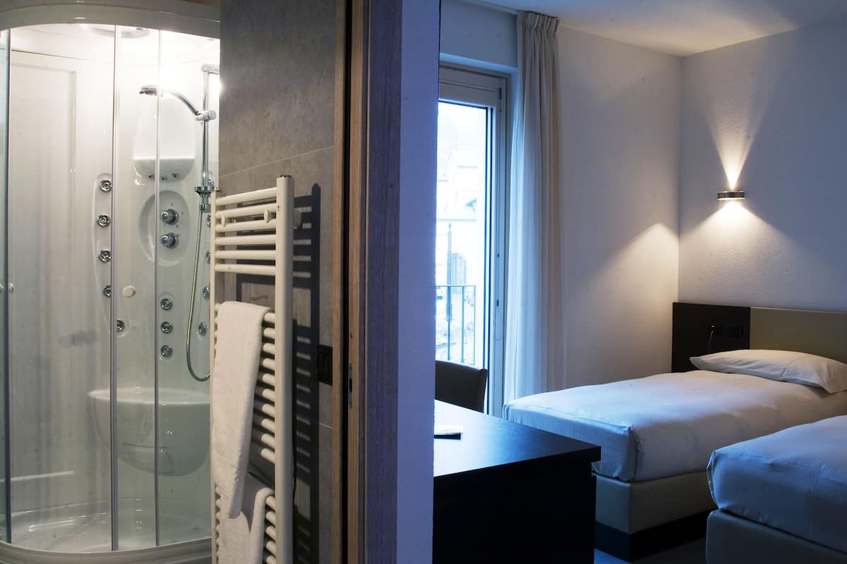 Une chambre d’hôtel avec une douche en verre, un lit avec du linge de lit blanc et une table de chevet.