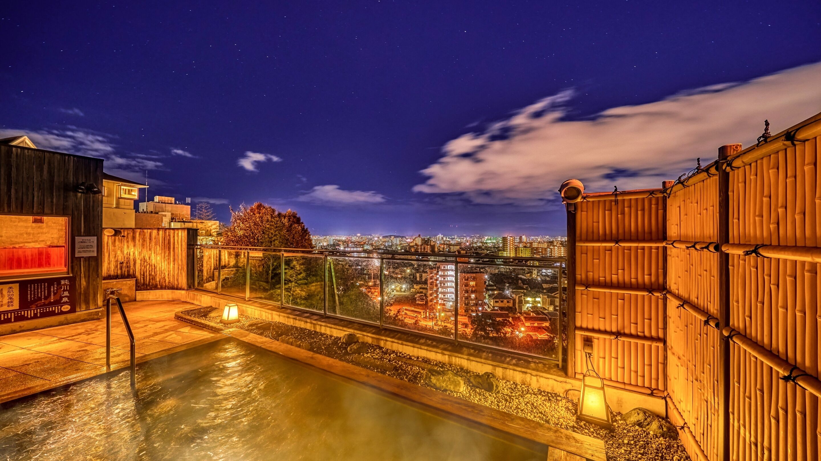 A rooftop terrace with a hot spring, city view, and traditional wooden structures.