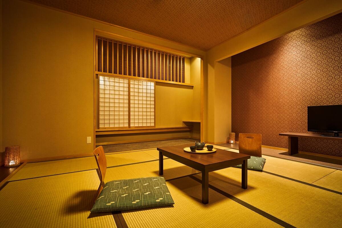 Una tradizionale stanza giapponese con pavimento in tatami, un tavolino, un televisore e un paravento shoji.