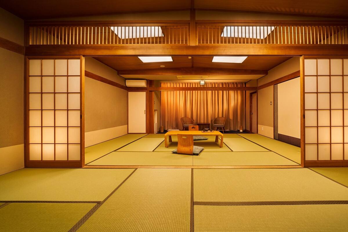 Una tradizionale stanza giapponese con pavimentazione in tatami, porte scorrevoli e un tavolino con cuscini.