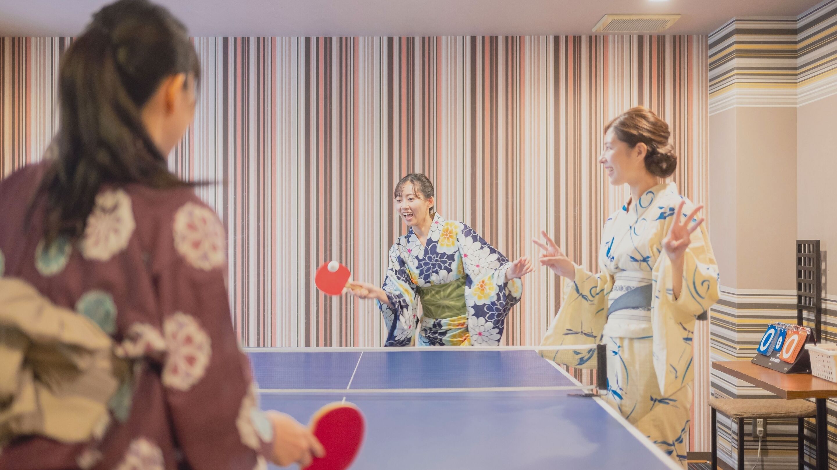 Et værelse med et ping pong-bord, stribet tapet og et bord med ting på.