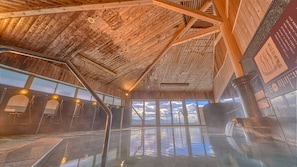 A wooden interior with a glass pool, metal railings, and a view of the sky.