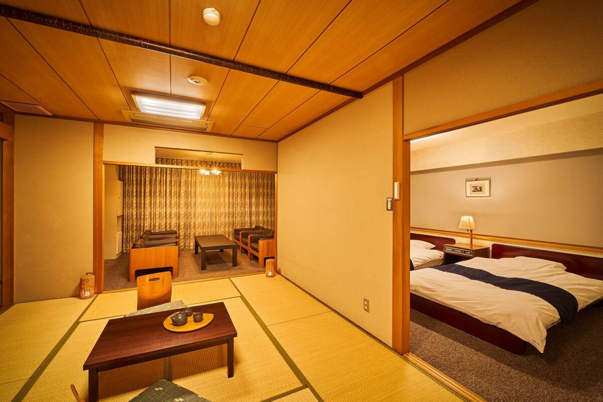 Una camera d'hotel in stile tradizionale giapponese, con pavimento in tatami, un letto futon, un tavolino con un set da tè e una televisione.