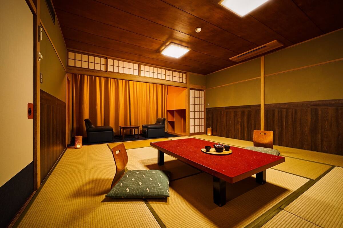 Una stanza tradizionale giapponese con pavimento in tatami, un tavolino con superficie rossa e un portascoperto con tende.