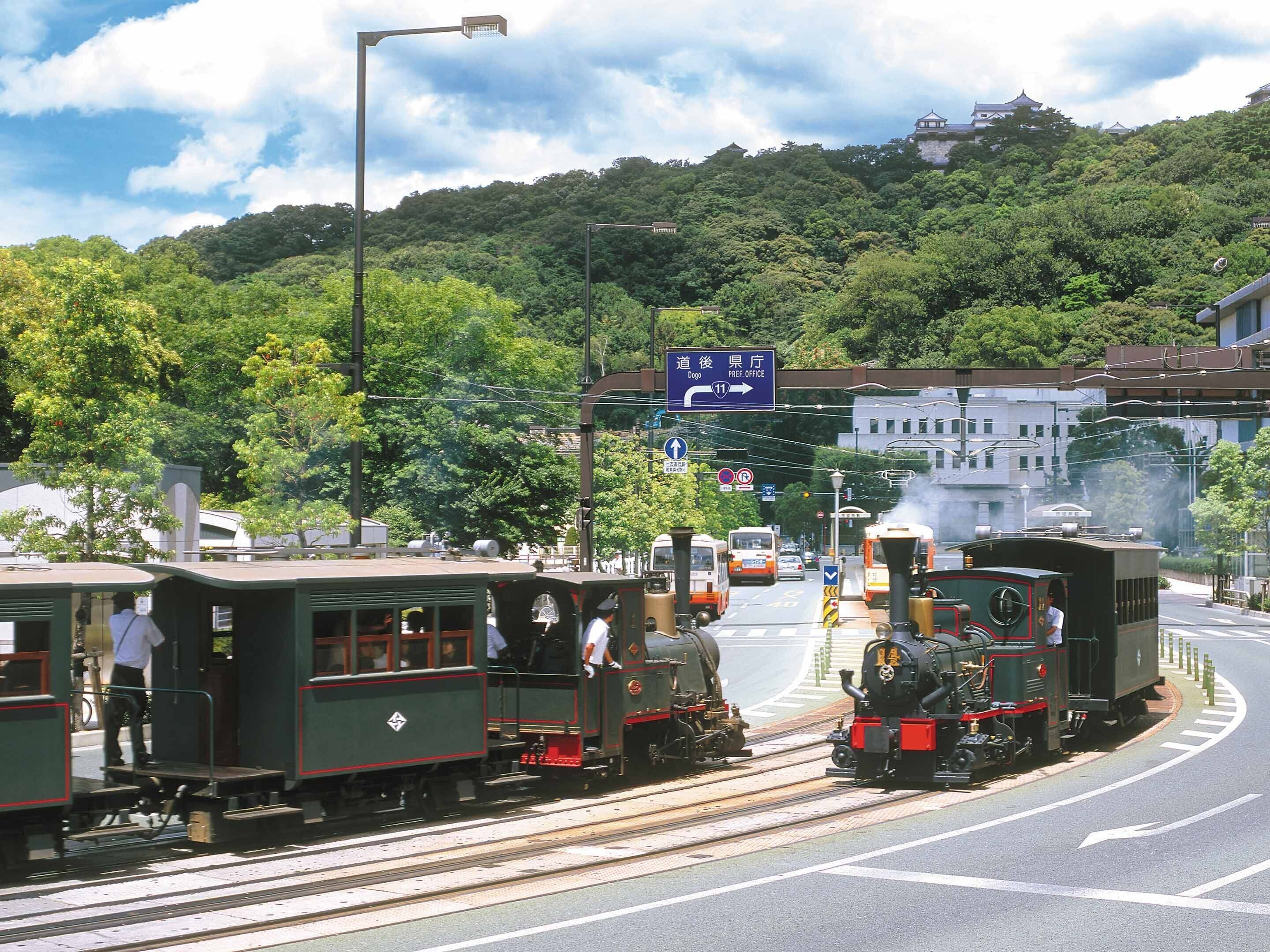 A vintage steam train on tracks with a modern cityscape in the background.