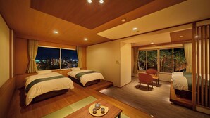 A hotel room with two beds, a dining table with a teapot and cups, a chair, and large windows offering a city view. - Ooedo Onsen Monogatari Dogo (Matsuyama)