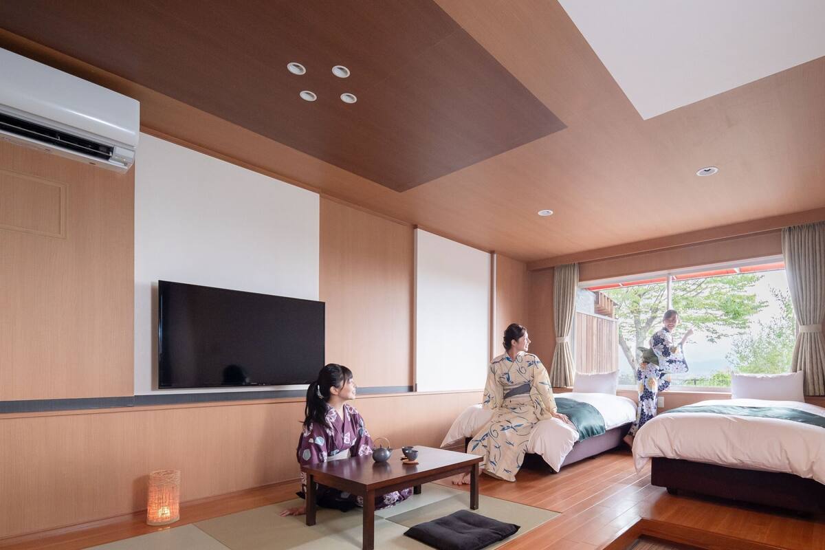Una tradizionale stanza in stile giapponese, con pavimento in tatami, un tavolino basso, un letto con futon e un televisore a parete.