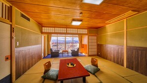 A traditional tatami room with a low table, two chairs, and a view of a cityscape through large windows. - Ooedo Onsen Monogatari Dogo (Matsuyama)
