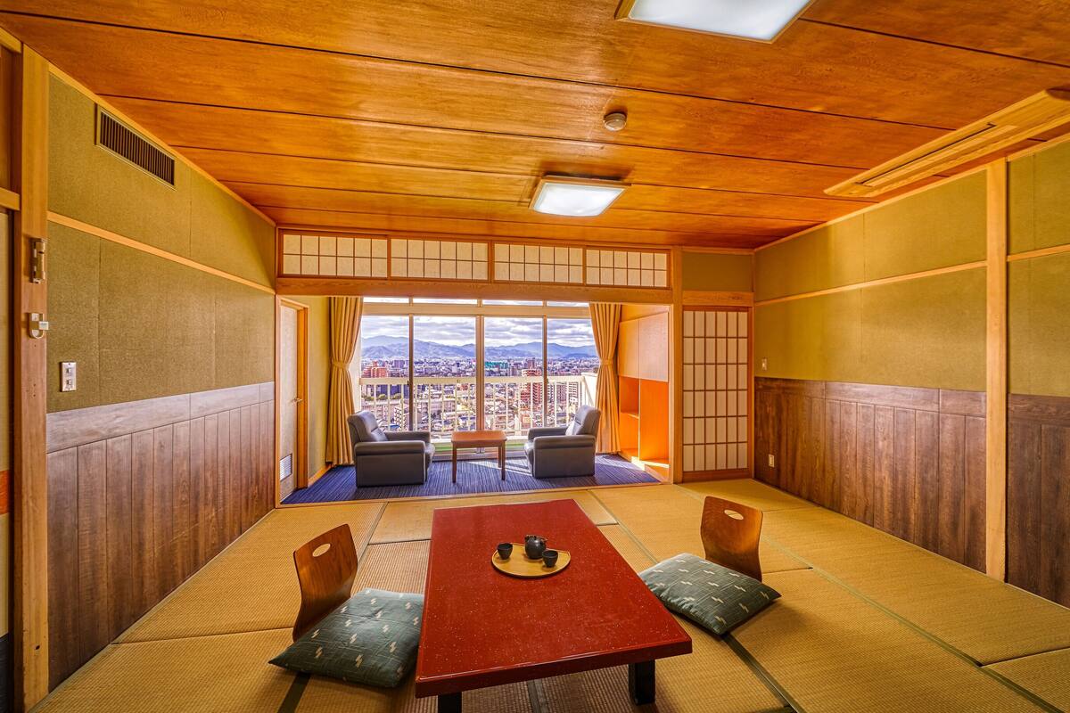 Una stanza con tatami, un tavolino basso, cuscini e vista sulla città.
