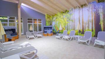 Un salon intérieur lumineux, avec des fauteuils blancs, un plafond en bois et une fresque représentant une forêt.