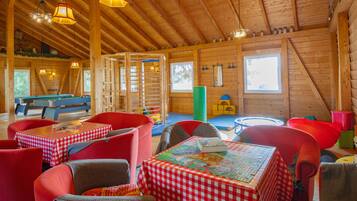 L’intérieur d’un chalet en bois chaleureux et accueillant, avec un billard, des tables à carreaux rouges et blancs et des chaises rouges.