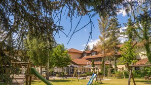 A playground with slides and swings, surrounded by trees and buildings with red-tiled roofs. - Ferien Hotel Spree-Neiße (Neuhausen/Spree)