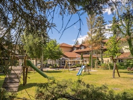 A playground with slides and swings, surrounded by trees and buildings with red-tiled roofs.
