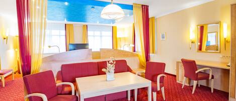 A hotel room with a bed, a desk, a chair, a table, and a large window.