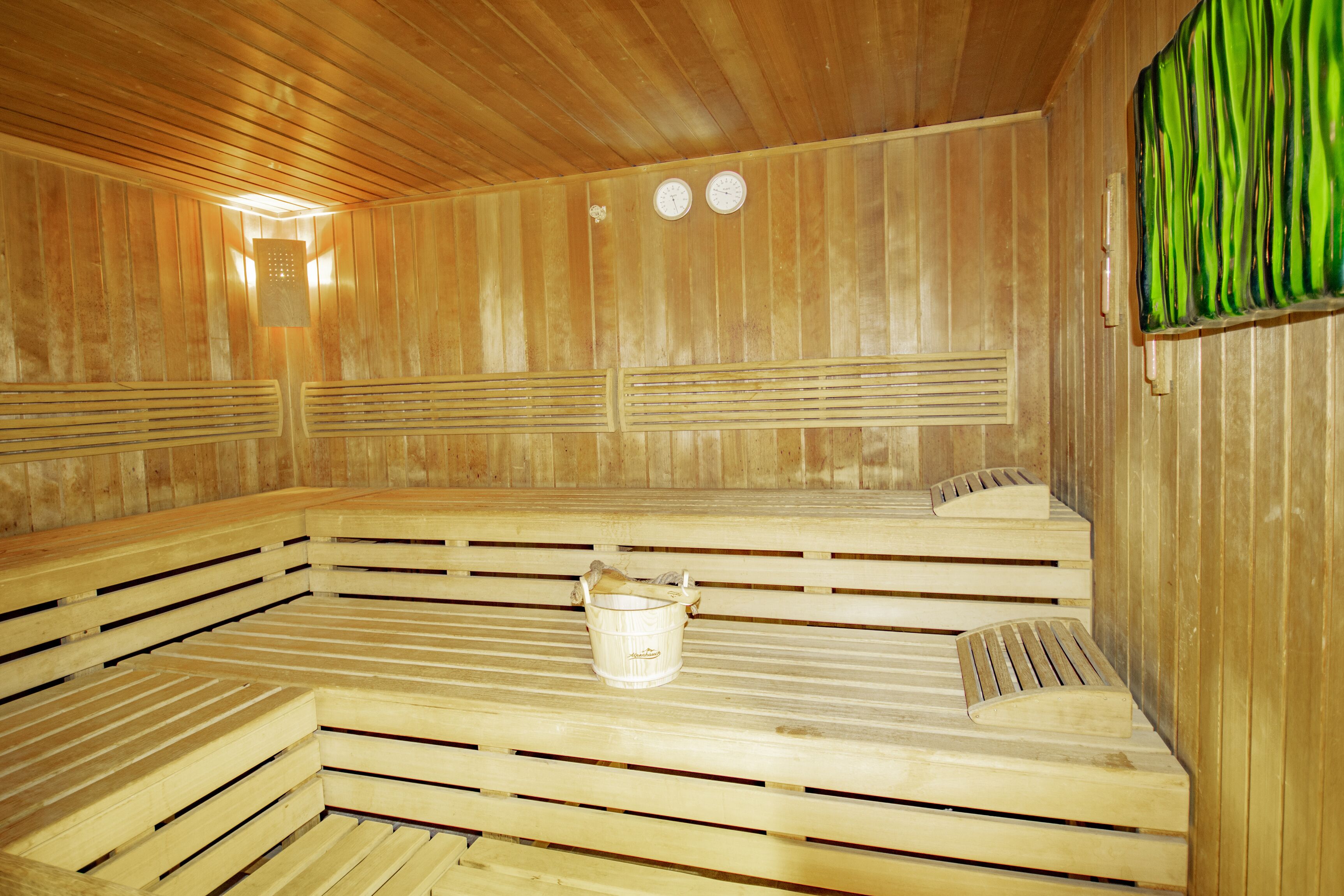 Eine Holzsauna mit Bänken, einem Eimer und zwei Uhren an der Wand.