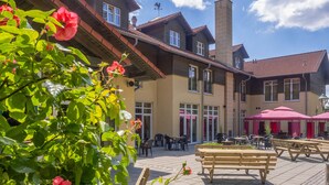 A courtyard with outdoor seating, a wooden bench, and a building with multiple windows and a chimney. - Ferien Hotel Spree-Neiße (Neuhausen/Spree)
