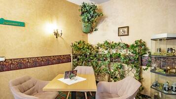 A room with a table and two chairs, a green sign, a wall-mounted light fixture, a potted plant, and a glass display case with items.