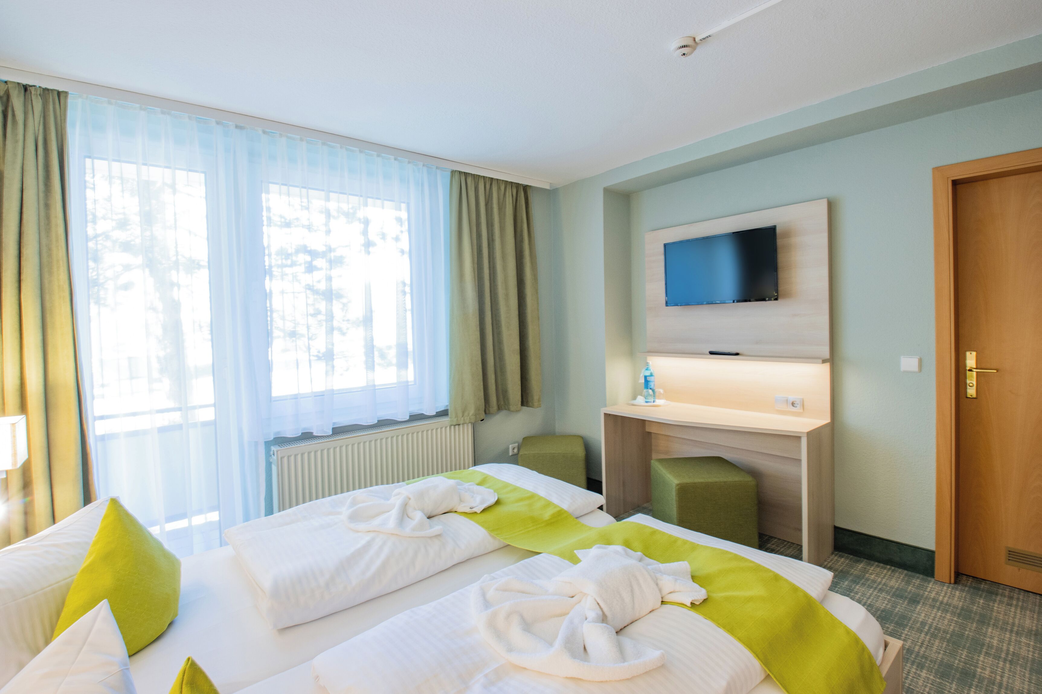 Una habitación de hotel con dos camas, un televisor montado en la pared, un escritorio y una puerta.