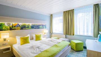 Habitación de hotel con cama, escritorio, silla, ventana con cortinas y un cuadro en la pared.