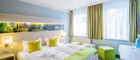 Habitación de hotel con cama, escritorio, silla, ventana con cortinas y un cuadro en la pared.