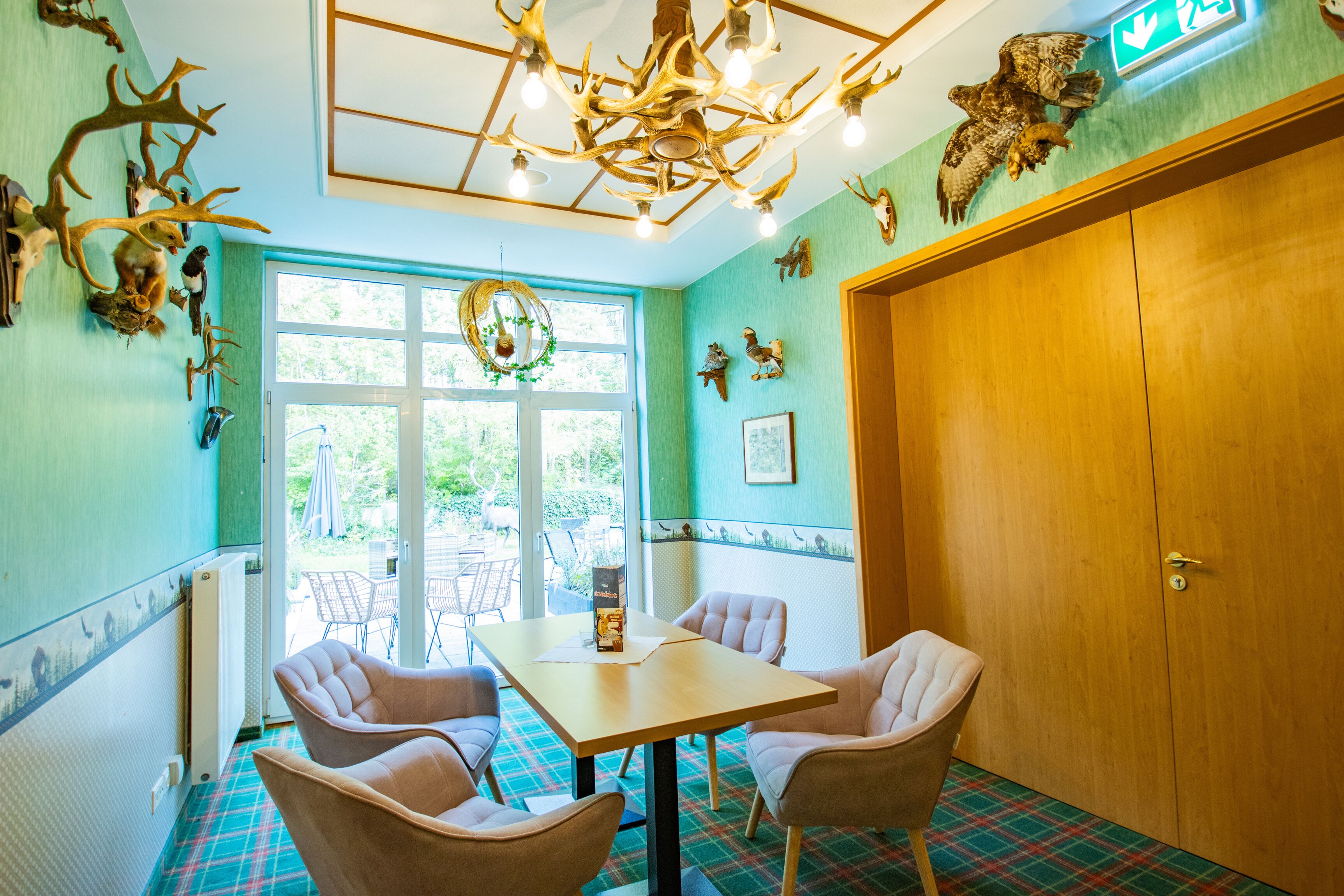 A room with a plaid carpet, a table with chairs, a wooden door, and wall-mounted animal horns and an owl.