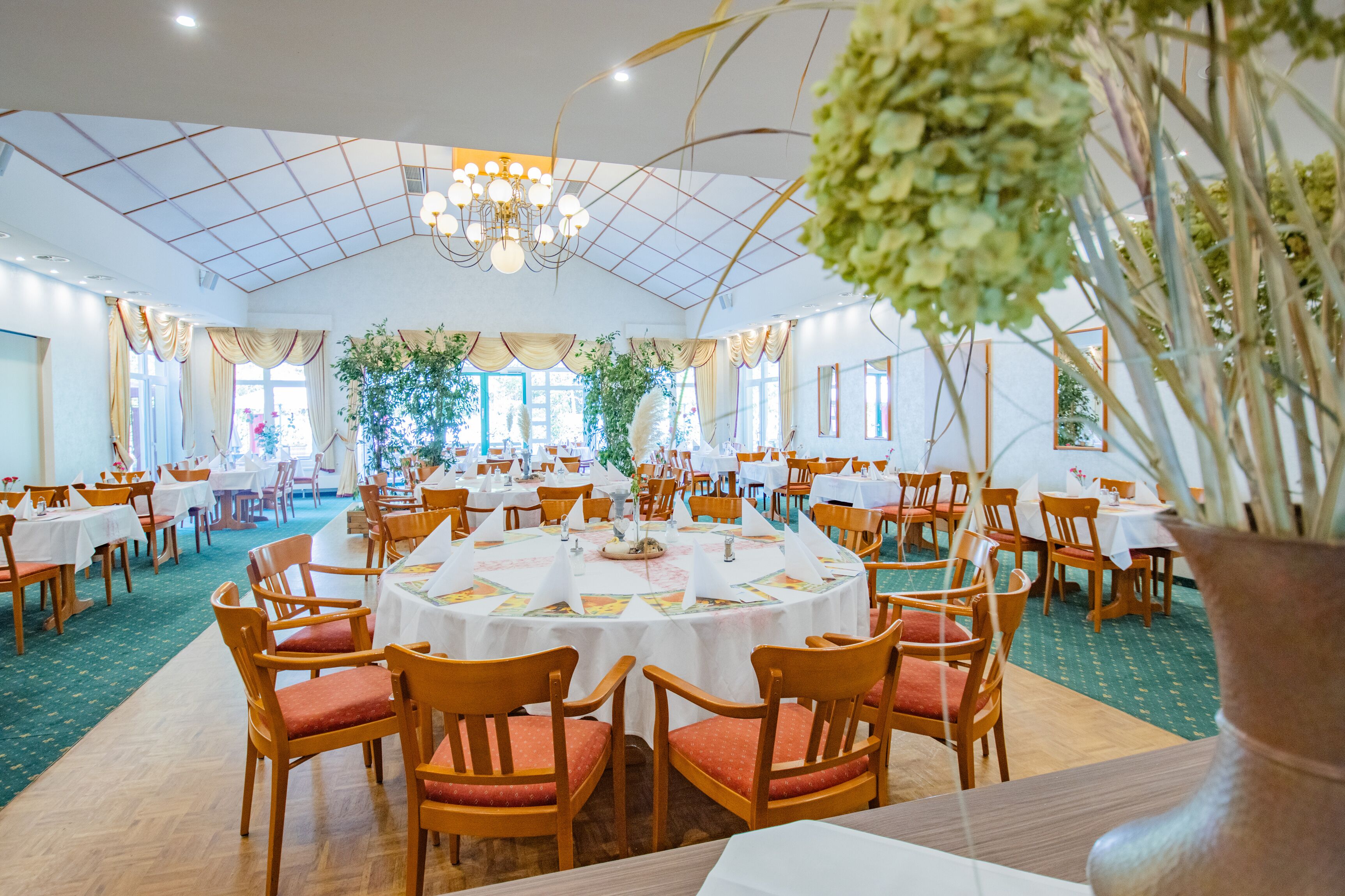 A banquet hall with round tables, wooden chairs, and a chandelier.