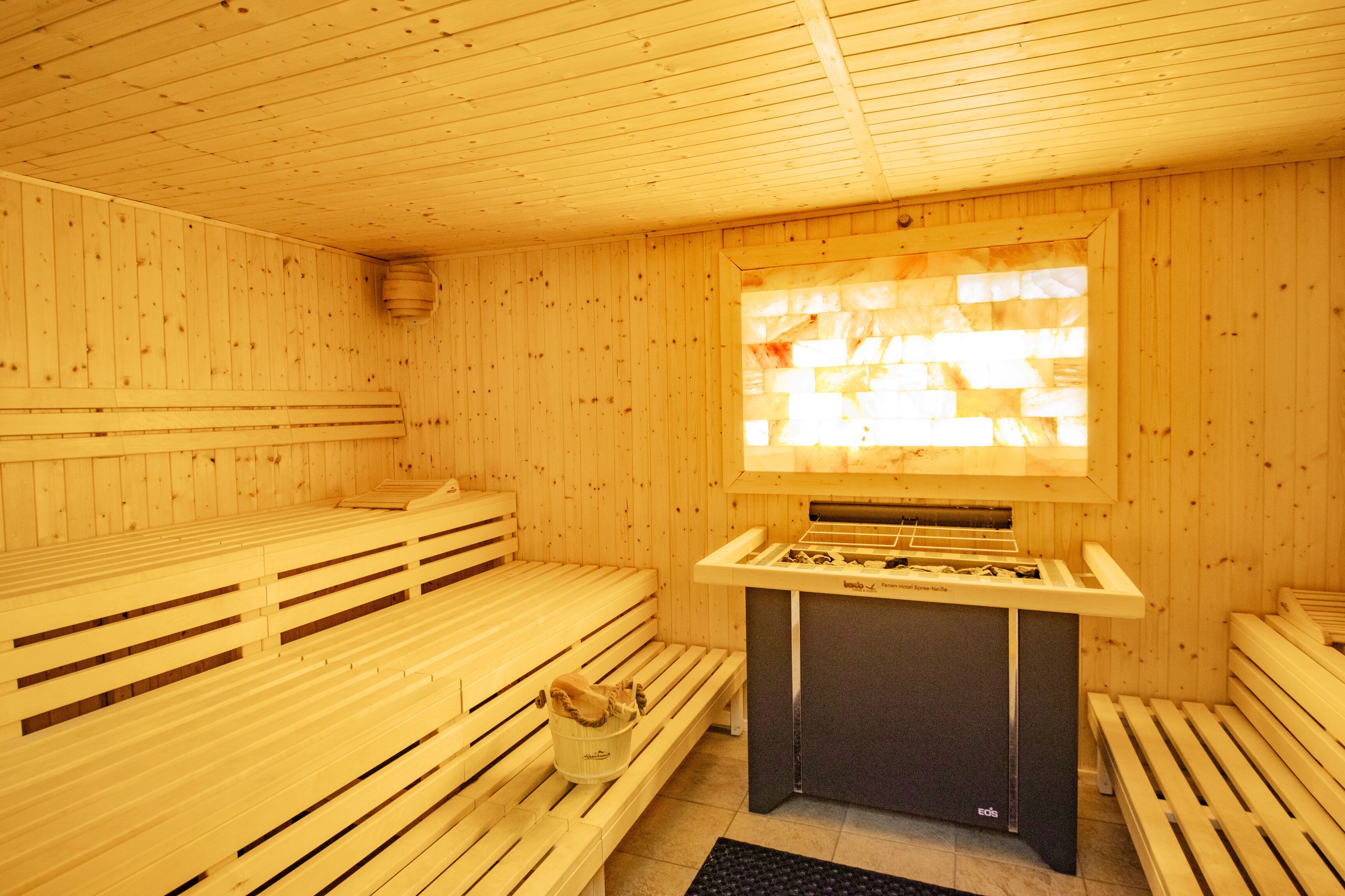 Ein Saunaraum mit Holzbänken, einer Bank mit Handtuch und einer Saunaheizung.