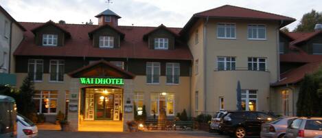A hotel with a traditional European architectural style, featuring a prominent entrance with a sign, multiple windows, and a parking area with cars.