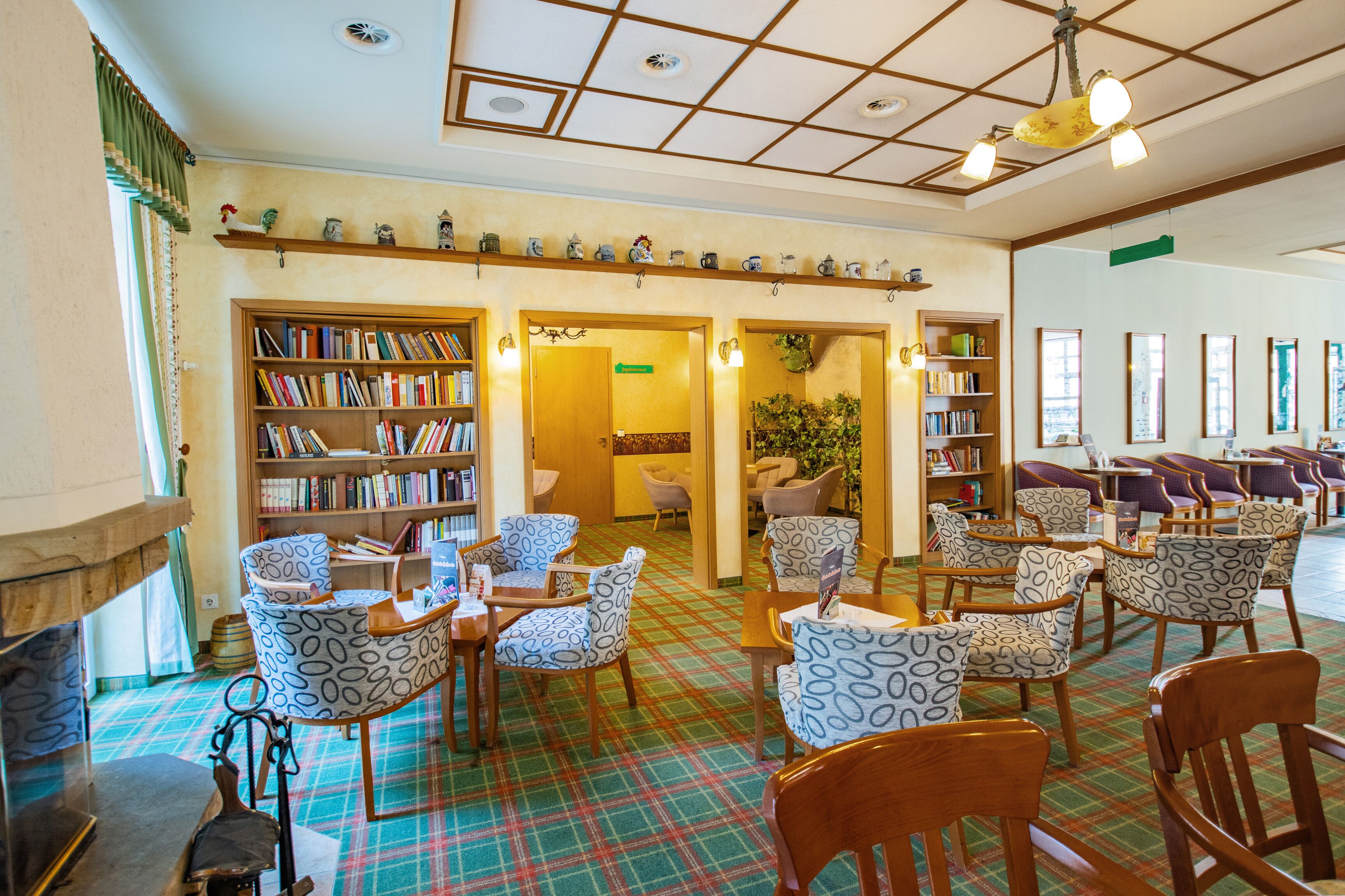A library with bookshelves, patterned chairs, and a plaid carpet.