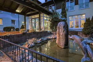 A building with a pond, a large rock, and a dolphin statue.