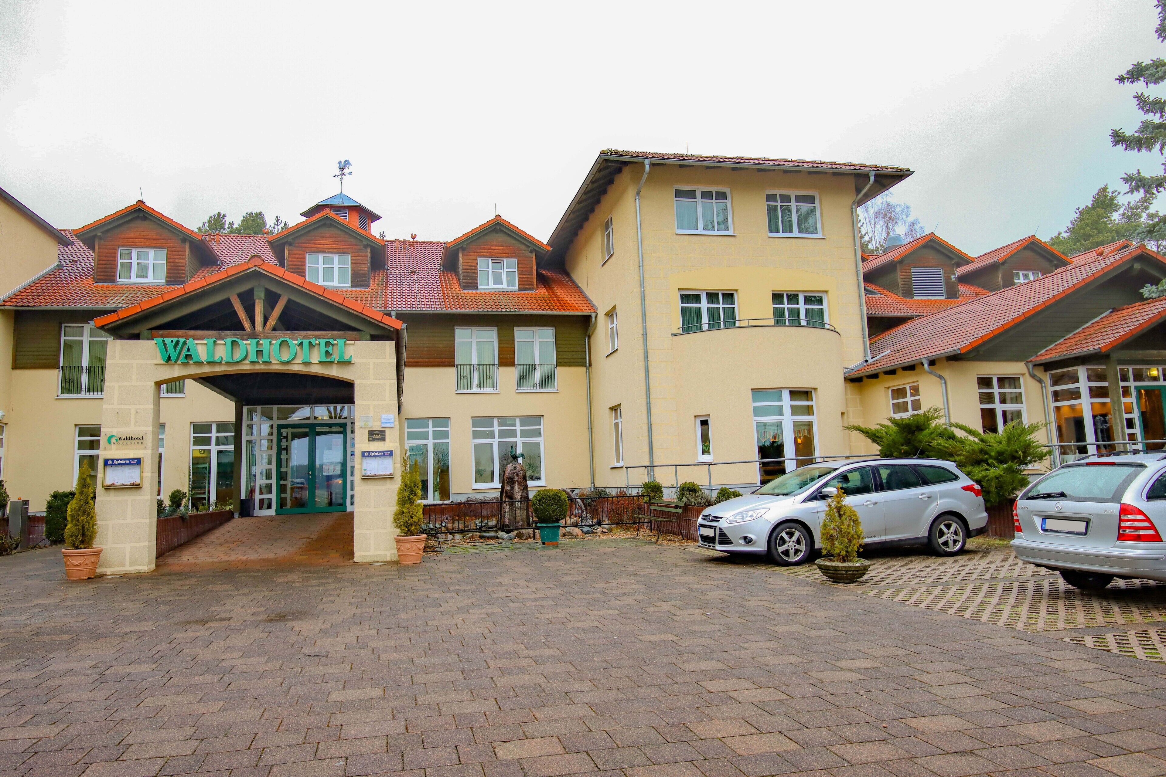 A hotel with a prominent entrance, multiple windows, and a parking area with cars.