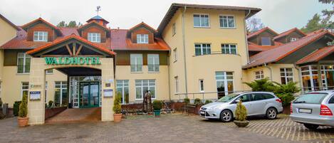 A hotel with a prominent entrance, multiple windows, and a parking area with cars.