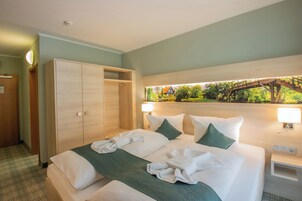 A hotel room with a bed, a wardrobe, a nightstand, and a view of a bridge and greenery.