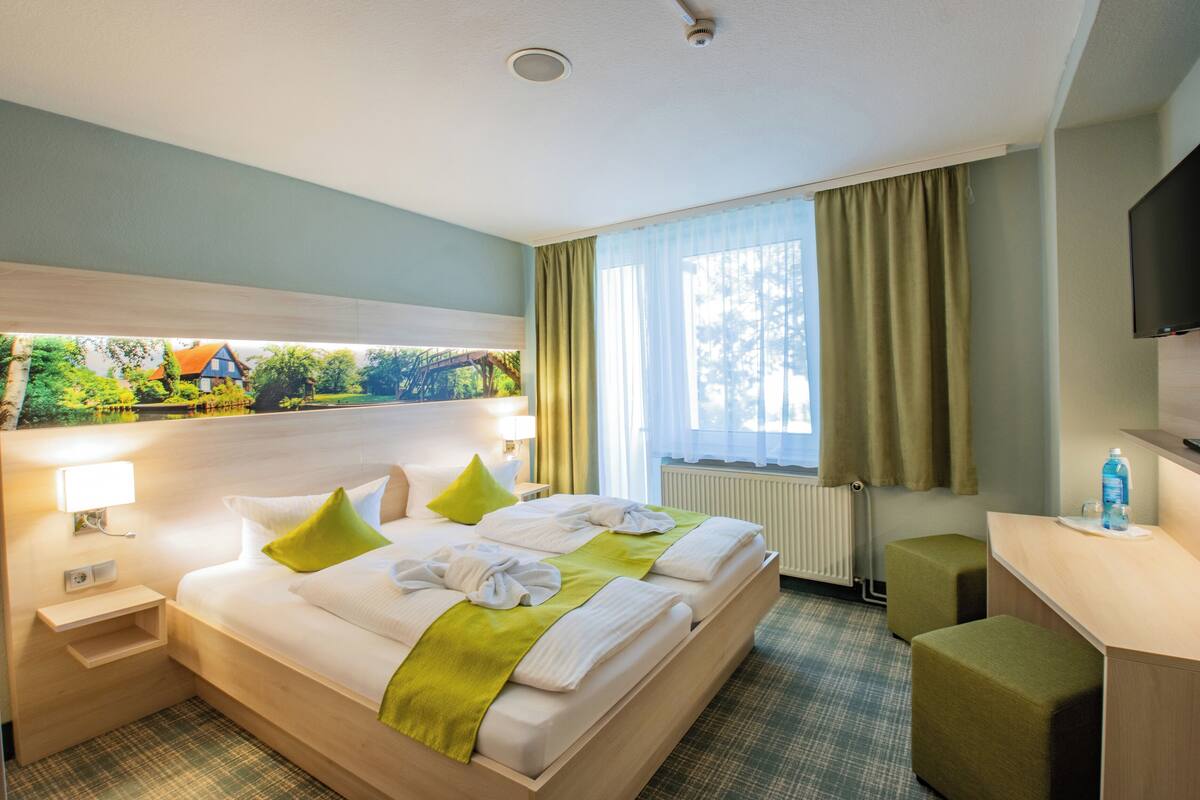 A hotel room with a bed, a desk, a chair, a television, and a window with curtains.