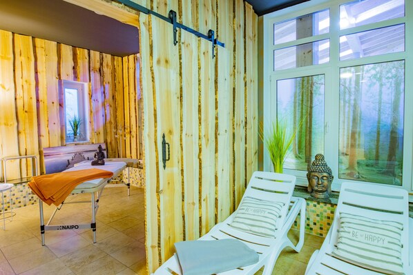 Une pièce aux murs en bois, une fenêtre donnant sur la forêt, un espace dédié à la méditation et une table de massage.