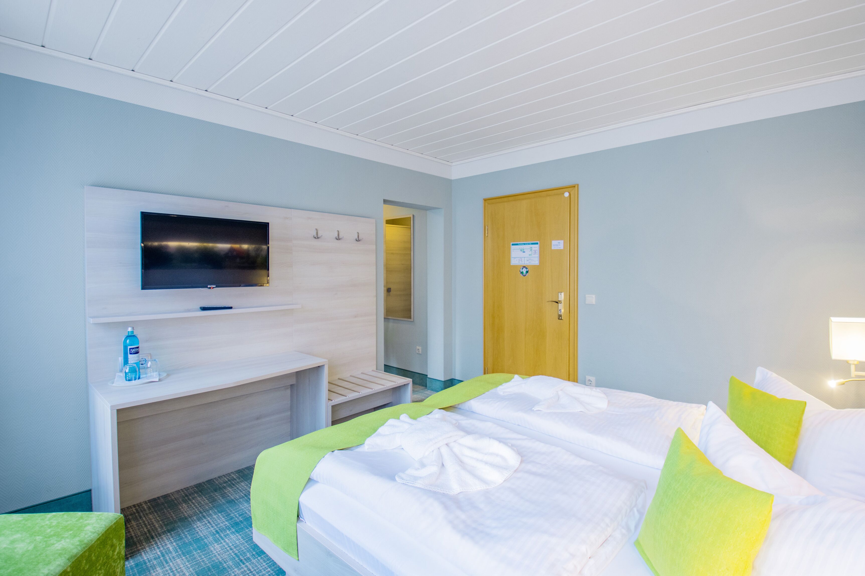 A hotel room with a bed, a TV mounted on the wall, a desk, and a door.