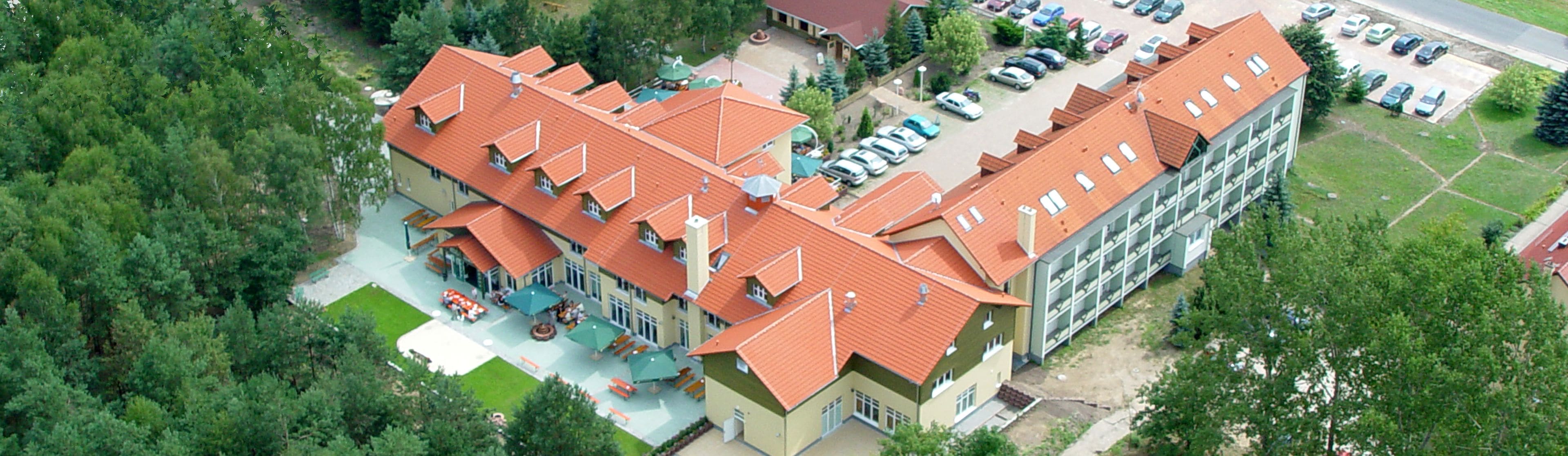 An aerial view of a hotel with multiple buildings, a parking lot, and surrounding greenery.