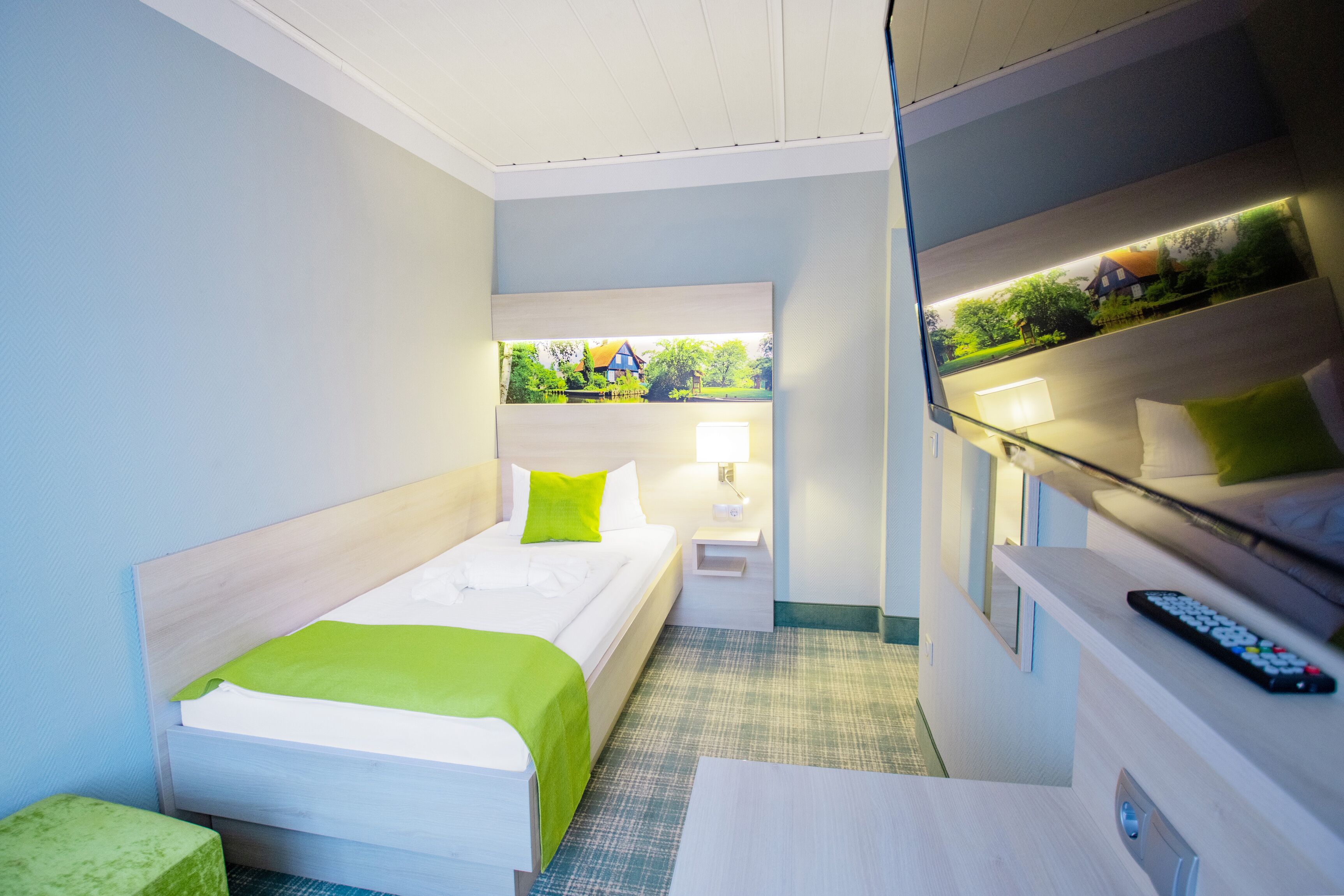 Habitación de hotel con cama, mesita de noche, lámpara y vistas a zonas verdes a través de una ventana.
