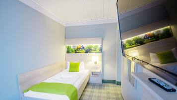 Habitación de hotel con cama, mesita de noche, lámpara y vistas a zonas verdes a través de una ventana.