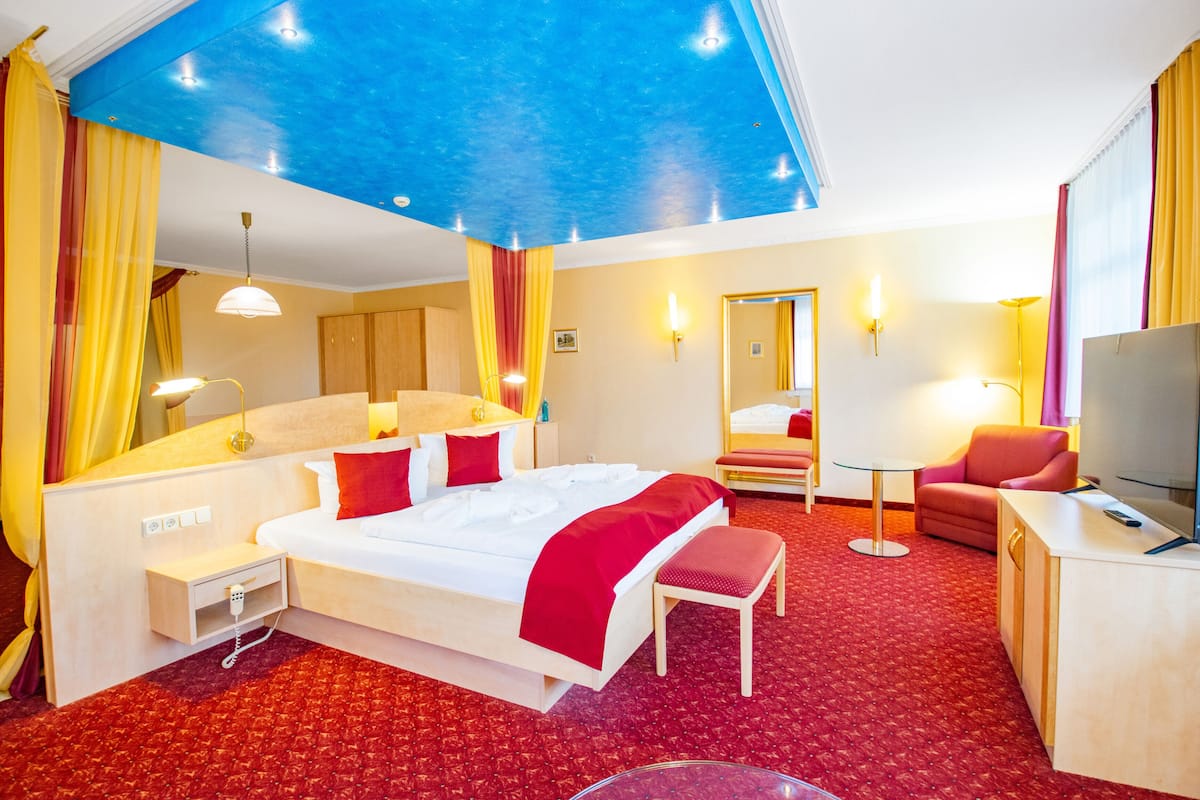 A hotel room with a large bed, a desk, a chair, a TV, and a mirror.