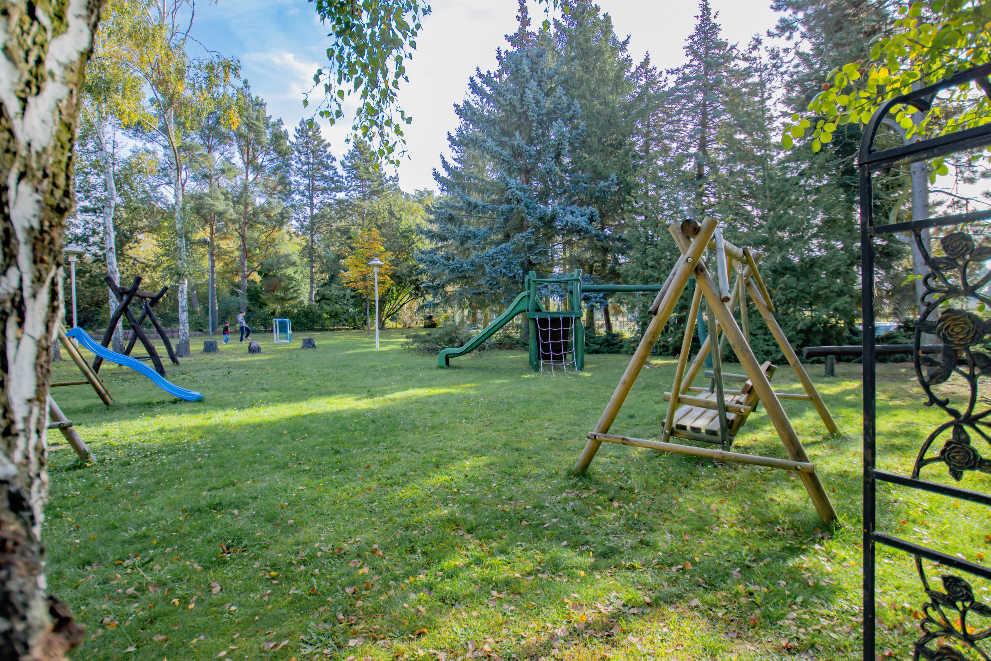 A playground with swings and slides, surrounded by trees and grass.