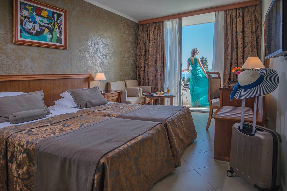 A hotel room with two beds, a sitting area, a balcony, and a view of the outdoors.