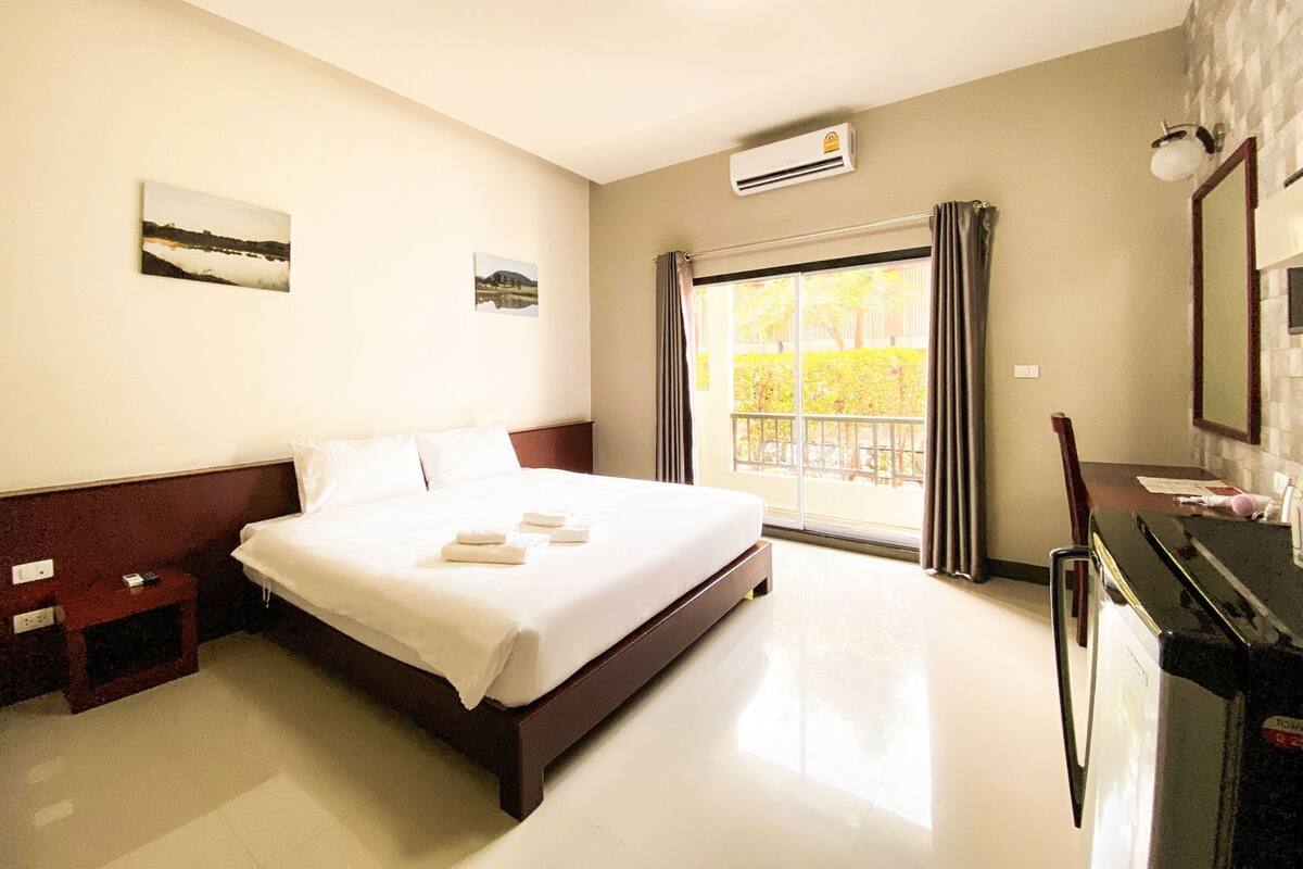 Een hotelkamer met een groot bed, een bureau, een stoel, een airconditioner en een raam met gordijnen.