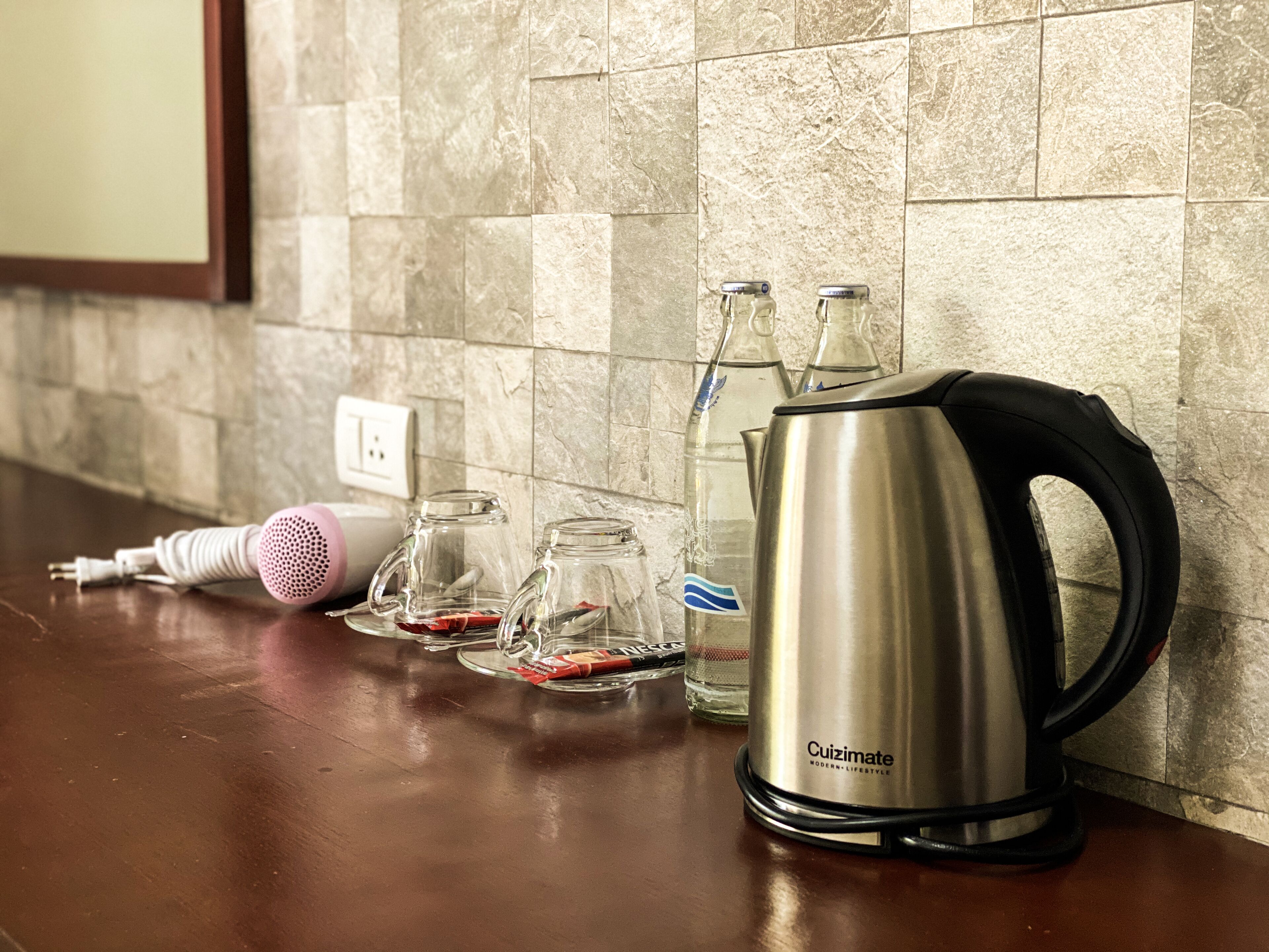 A kitchen counter with a kettle, two glass mugs, a water bottle, and a pink hairdryer.