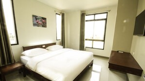 Een hotelkamer met een groot bed, een nachtkastje, een bankje en een aan de muur bevestigde televisie.
