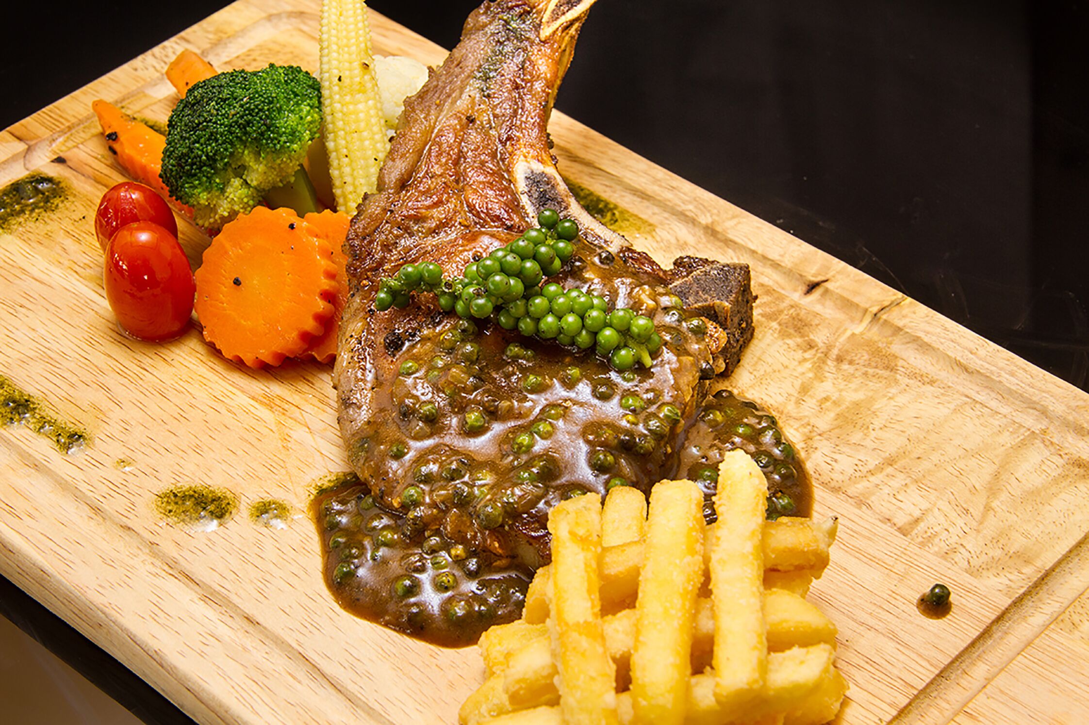 Une planche à découper en bois sur laquelle on a disposé un morceau de cuisse de canard rôtie, des petits pois et une portion de frites.
