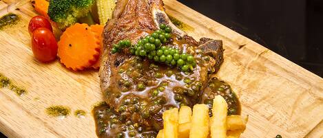 Une planche à découper en bois sur laquelle on a disposé un morceau de cuisse de canard rôtie, des petits pois et une portion de frites.