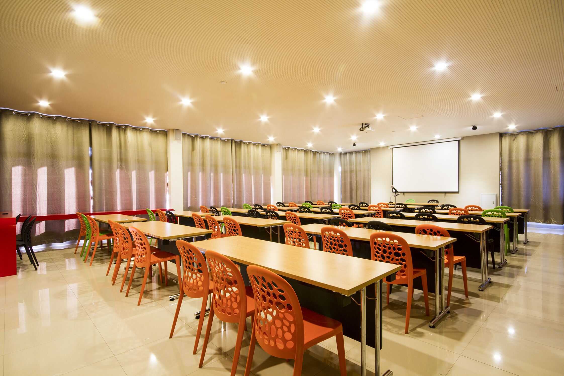 A conference room with multiple tables and chairs, a projector screen, and a large window with curtains.