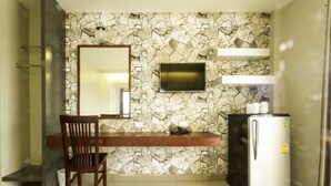 Een kleine kitchenette met een betegelde achterwand, een flatscreen televisie, een koelkast en een houten eettafel met een stoel.