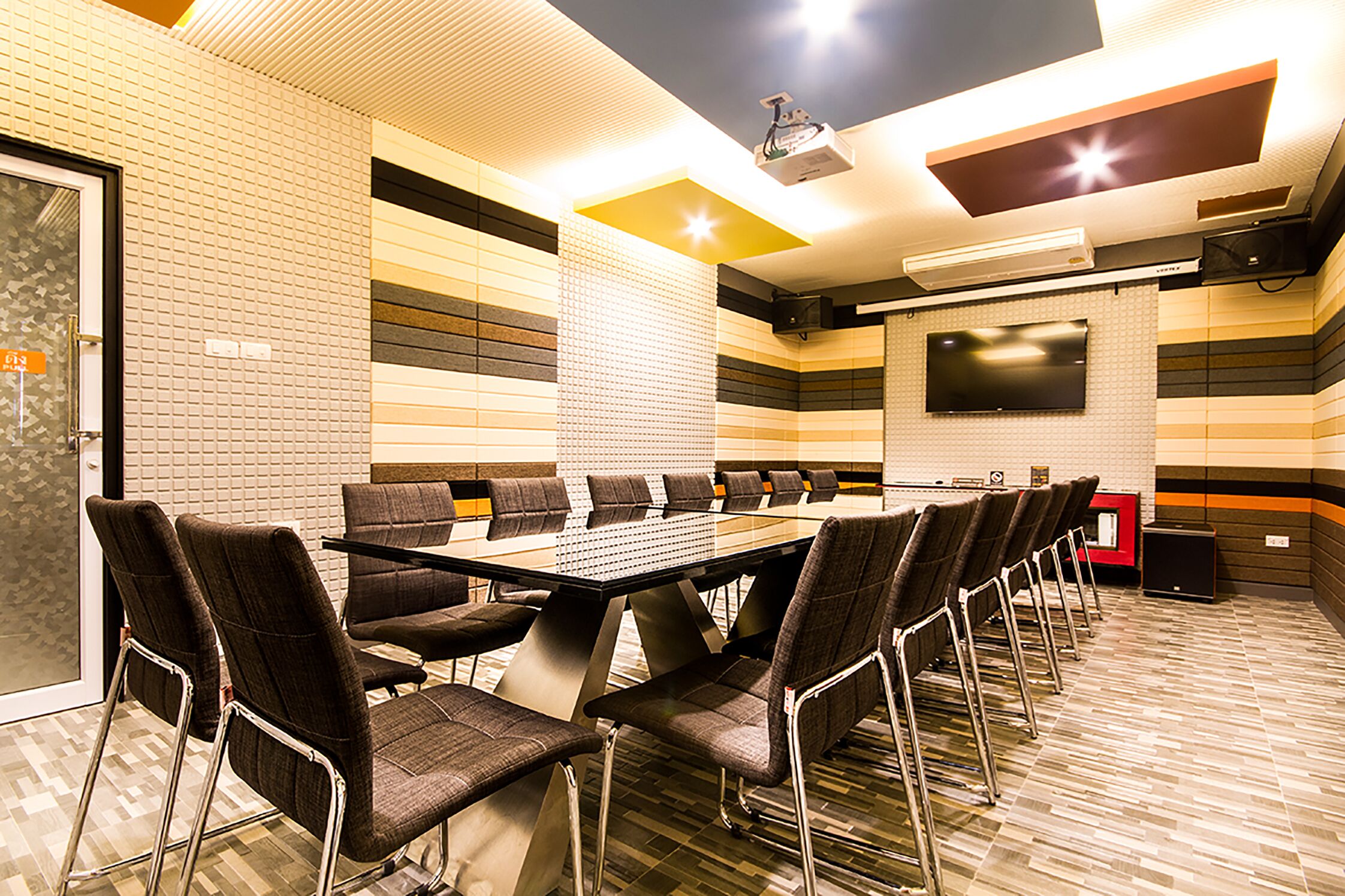 A conference room with a long table and chairs, a flat-screen TV, and a ceiling-mounted projector.
